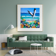 Load image into Gallery viewer, Colourful painting of a sea eagle flying over a beach with flowers and waves, displayed on a living room wall