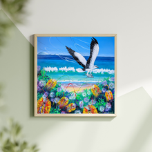 Load image into Gallery viewer, Colourful painting of a sea eagle flying over a beach with flowers and waves, displayed on a wall
